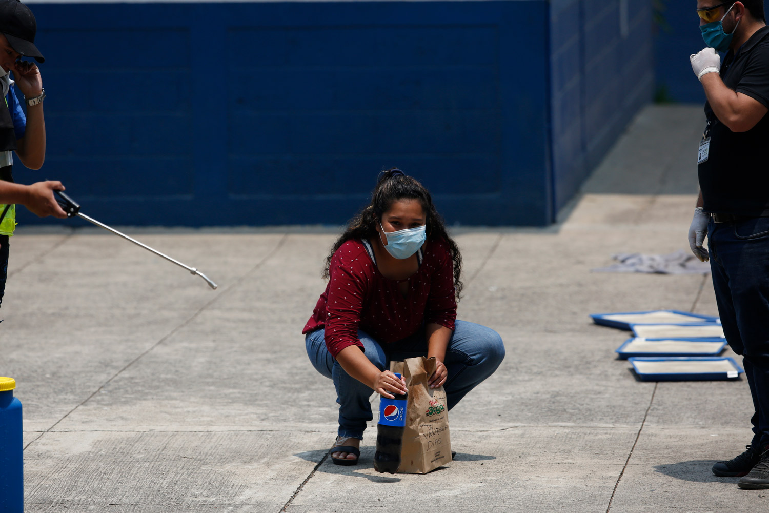 La deportada guatemalteca Vanessa Díaz mira a su familia mientras recoge la comida que le trajeron, en el lugar donde tienen que pasar la cuarentena los retornados de EEUU